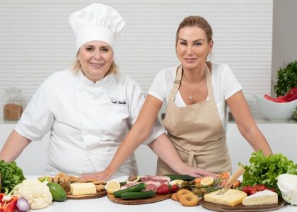 Two female chefs with variety of fresh ingredients in a kitchen setting, showcasing culinary preparation.